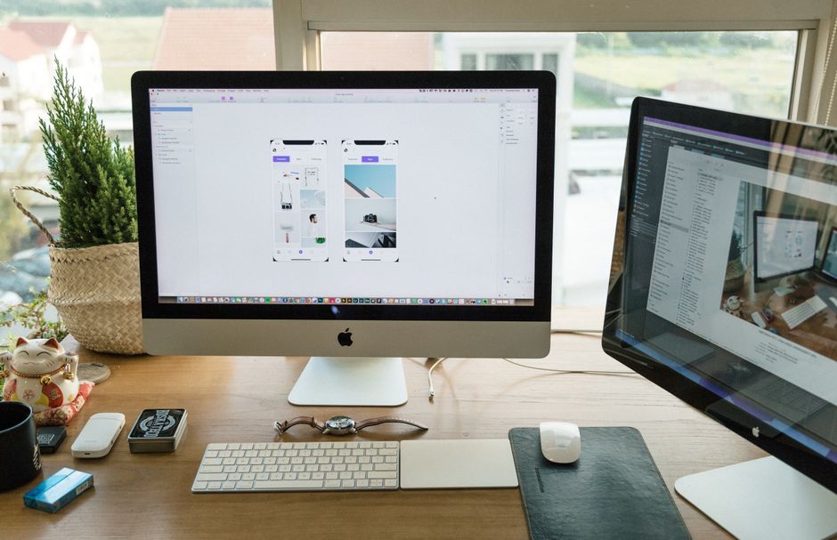 Um escritório moderno bem organizado com Apple iMac e múltiplos monitores em um ambiente de trabalho iluminado.