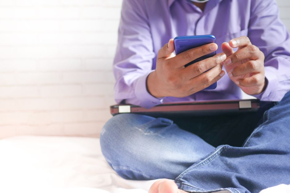 Ambiente casual com um homem usando um smartphone dentro de casa, focando em tecnologia e relaxamento.