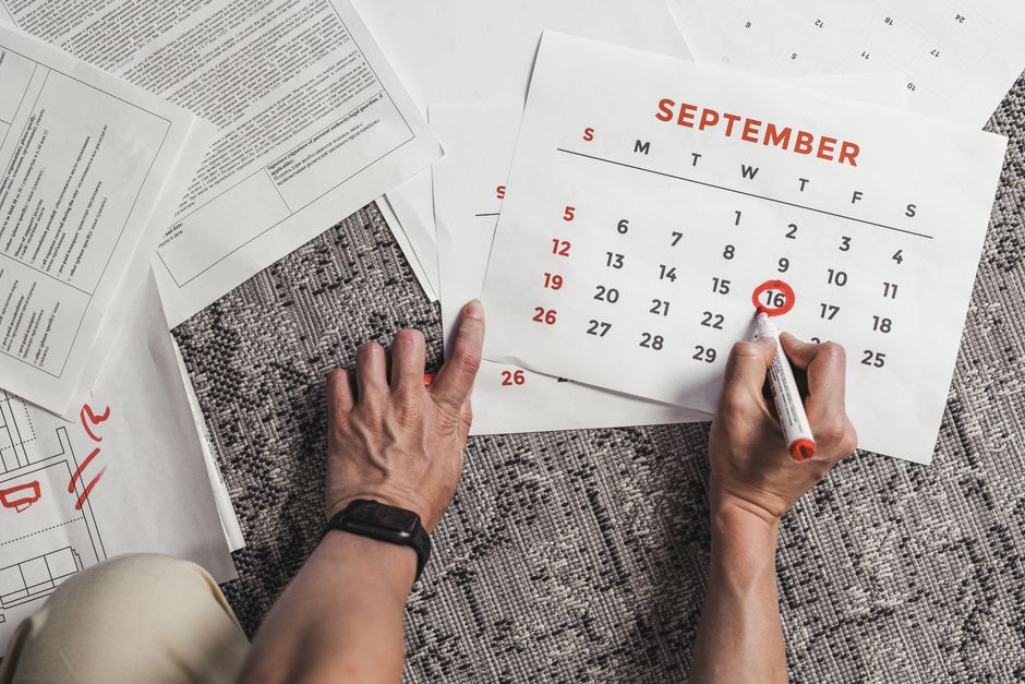 Mãos segurando um calendário com datas de setembro circuladas, cercado por documentos em um tapete.