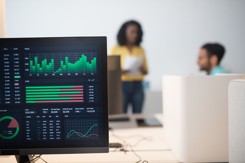 Escritório moderno com telas de trading financeiro e uma equipe diversa discutindo estratégias.