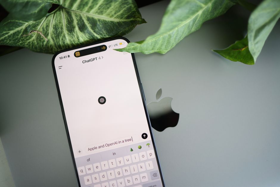 Um smartphone exibe uma interface do ChatGPT colocado em um laptop Apple em um ambiente com folhagens.