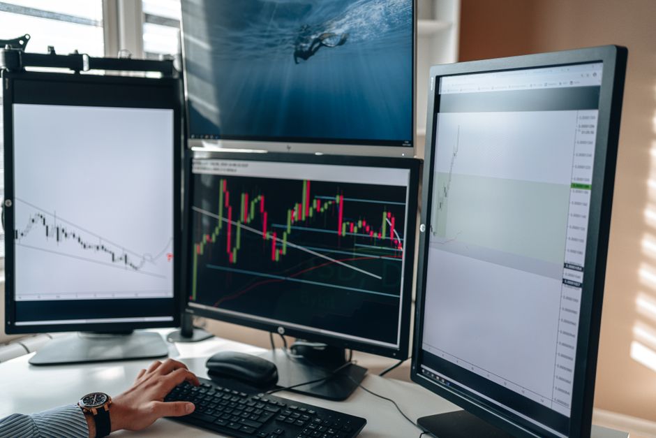 Um ambiente de home office com múltiplos monitores de negociação de ações exibindo gráficos e análise de dados.