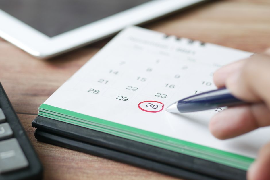 Close-up de uma mão marcando uma data em um calendário com uma caneta, enfatizando planejamento e agendamento.